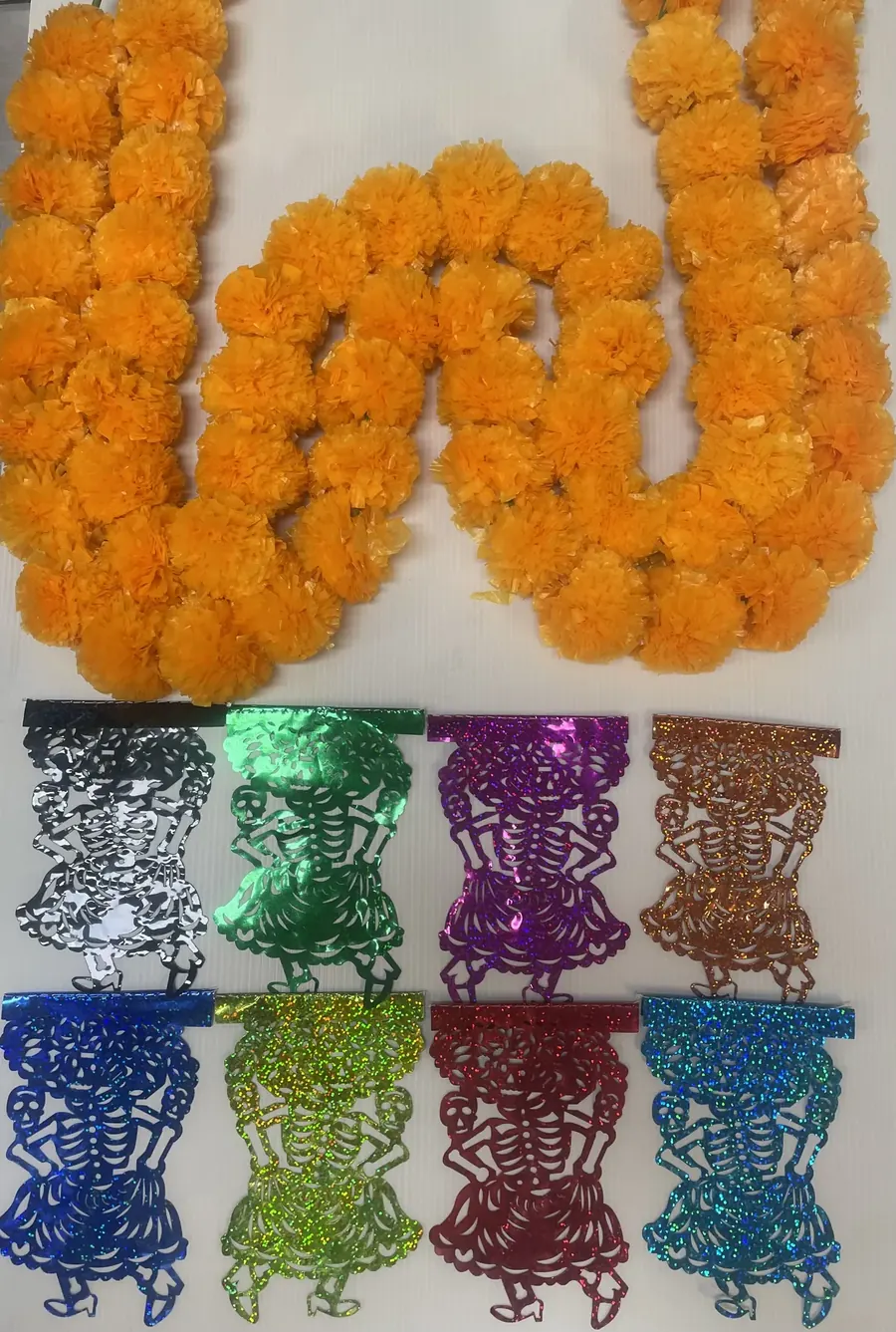 Artificial marigold garlands above a row of metallic papel picado skeleton banners