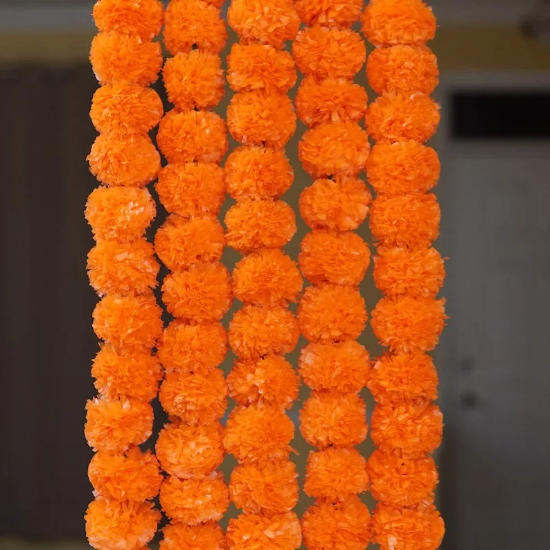 Strings of orange artificial marigold flowers hanging side by side